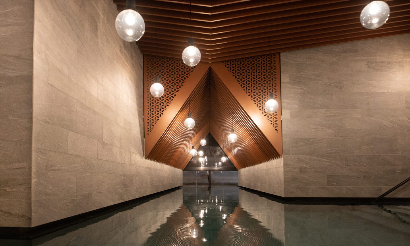 Indoor Pool  mit Blick Richtung Outdoor Pool, Kupferelemente und Lampen abgehängt von der Decke