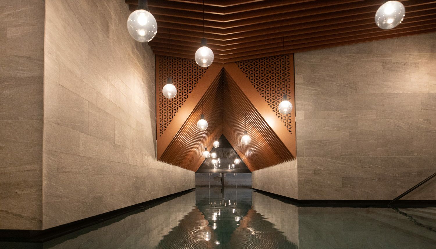 Indoor Pool  mit Blick Richtung Outdoor Pool, Kupferelemente und Lampen abgehängt von der Decke